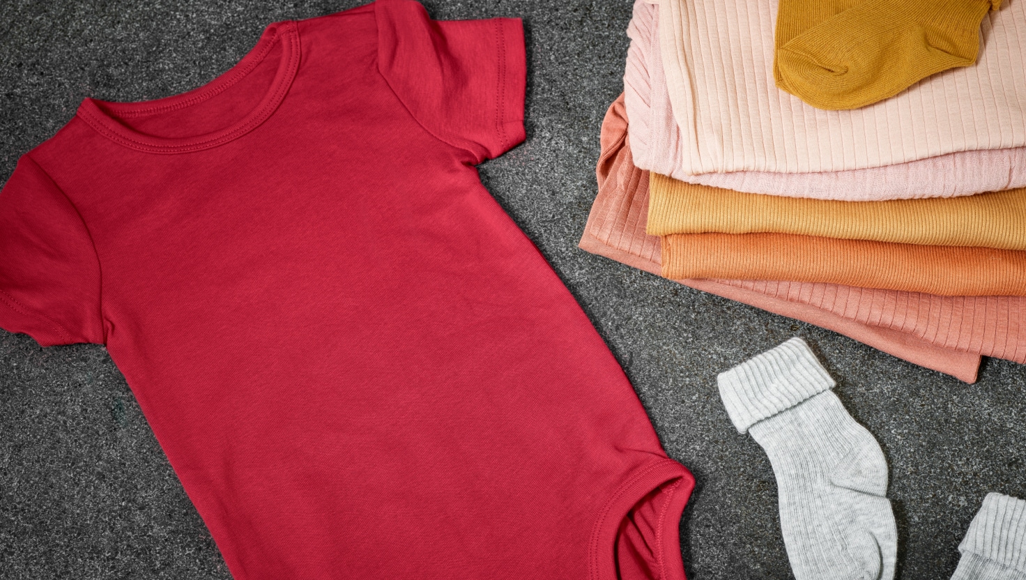 Pile of baby clothes lying on a grey carpet.