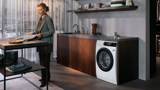 Woman folding sweater in laundry room in front of Washer Dryer